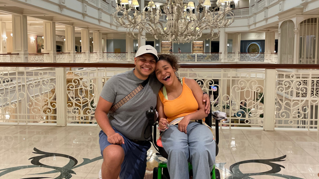 Happy young sibling couple posing at Grand Floridian entrance, young woman in wheelchair