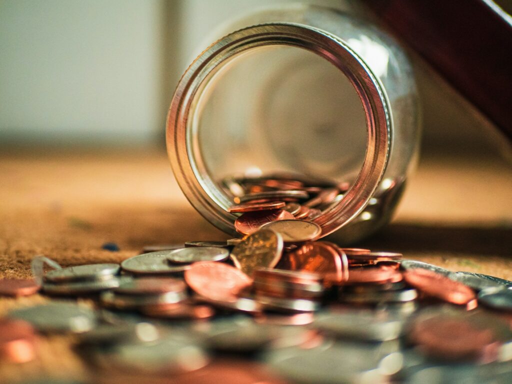 Open jar with coins and banknotes spilling onto the surface