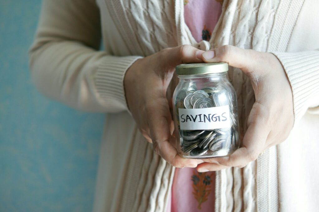 Woman smiling while holding a transparent savings jar filled with coins