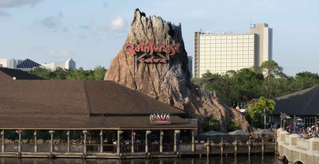 The captivating Rainforest Café Volcano at Disney Springs under a clear blue sky, symbolizing a perfect day for adventure with surrounding buildings complementing the iconic restaurant.